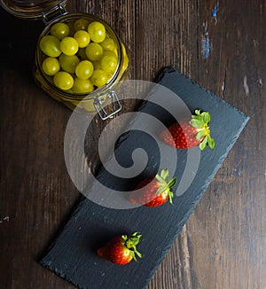 Still life fresh strawberries on slate plate with glass jar with fresh grapes on old basis overhead view
