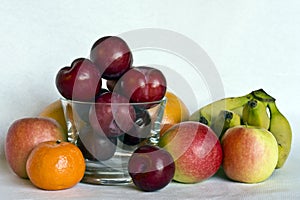 A still life of mixed fruit around and in a small glass bowl.
