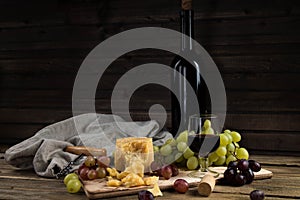 Still life from fruit, cheese and wine. The piece of hard cheese lies on a chopping board. Clusters of red and green mature grapes