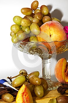 Still life with fruit peaches and grapes on a glass vase on a grey or silver background.