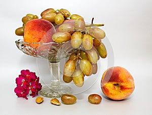 Still life with fruit peaches and grapes on a glass vase on a grey or silver background.