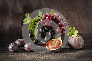 Still life with fruits: grape, fig, plum in the antique copper tin cup