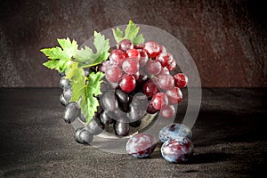 Still life with fruits: grape, plum in the antique copper tin cup