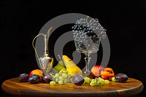 Still life with fruits on a round wooden table and black background.