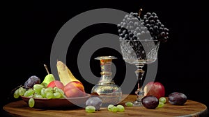 Still life with fruits on a round wooden table and black background.