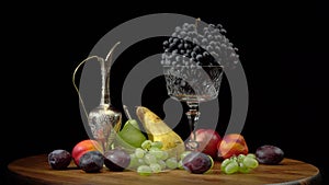 Still life with fruits on a round wooden table and black background.