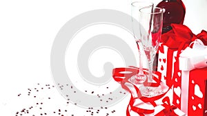 Still life with a gift box, red satin ribbon and two glasses of wine on a white background. Valentine`s Day card with copy space.