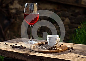 Still life with glass of red wine, coffee cup, beans in the sun