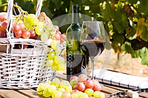 Still life with glass of red wine grapes and picnic basket on table
