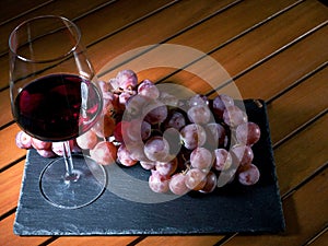 Still life, glass of red wine and red grapes on a slate plate and wooden table