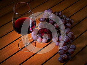 Still life, glass of red wine and red grapes on a wooden table. Warm tone