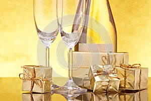 Still life with golden gift boxes, champagne bottle and empty champagne flutes on festive gold background