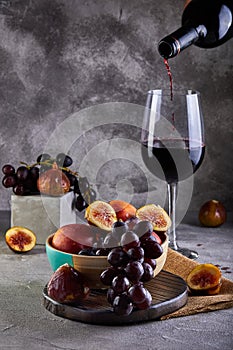 Still life of grapes, peaches, figs and glasses of red wine on a gray