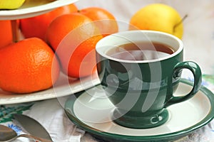 Still life of green cup of tea and orange tangerines.