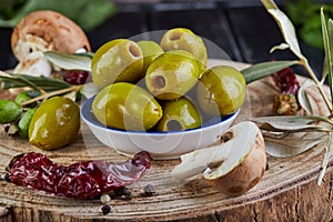 Still life of green fresh olives, red pepper and fresh mushrooms with olive tree leaves on a dark wooden close up