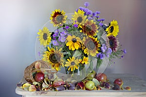 A spectacular bouquet of sunflowers in a vase and apples .