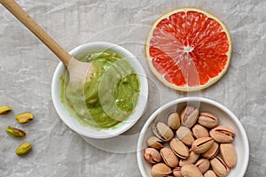 Still life of healthy food, pistachio paste, peeled and unpeeled salted pistachios, grapefruit, wooden spoon on a light background