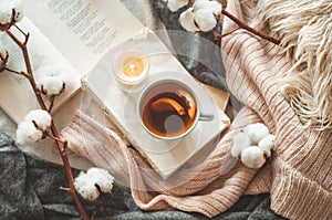 Still life in home interior of living room. Sweaters and cup of tea with a cone on the books. Read. Cozy autumn winter concept