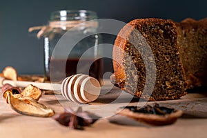 Still life with homemade cake, jar with honey and dipper, cinnamon, dried fruits, star anise on a wooden board. Small