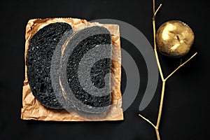 Still life image with charcoal bread on a black background with golden apple