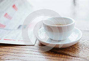 Still life image of cup of black coffee with fresh sport newspaper on the wooden table next to big coffee shop window