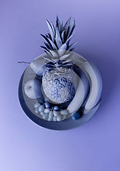 Still-life image of various fruits and a pineapple on a plate, with blue hues