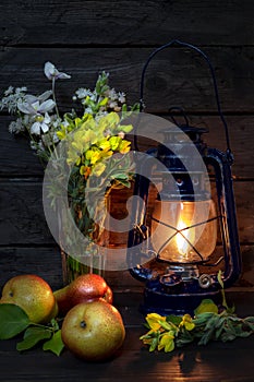 Still life with kerosene lamp, bouquet of wild flowers and ripe pear fruit