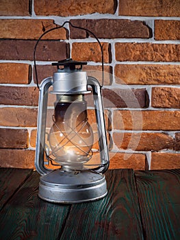 Still life kerosene lamp shines on wooden desktop stone brick background.