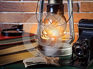 Still life kerosene lamp shines on wooden desktop stone brick background book camera.