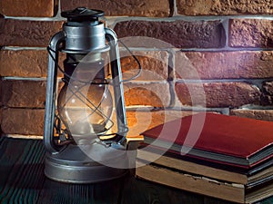 Still life kerosene lamp shines on wooden desktop stone brick background book camera.