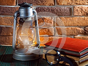 Still life kerosene lamp shines on wooden desktop stone brick background book camera.