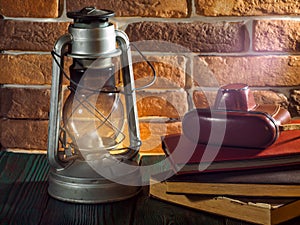 Still life kerosene lamp shines on wooden desktop stone brick background book camera.