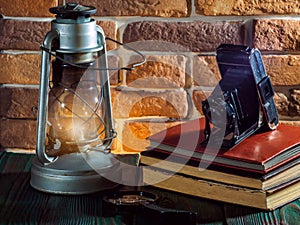 Still life kerosene lamp shines on wooden desktop stone brick background book camera.