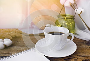 Still life kitchen details. Coffee cup, notepad, dried flowers and light glass on wooden desk.