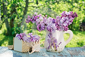 Still life with lilac in a jug, a casket, a shell on a wooden table