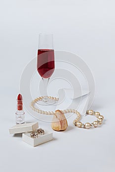 A still life with a little white envelop, a faded rose bud, a coral necklace, a lipstick, a box with the silver earrings