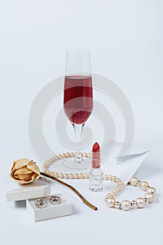 A still life with a little white envelop, a faded rose, a coral necklace, a lipstick, a box with the silver earrings