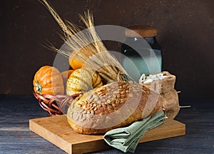 Still life with a loaf of pumpkin bread, spikelets, decorative pumpkins and a wooden board. World Bread Day