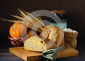 Still life with a loaf of pumpkin bread, spikelets, decorative pumpkins and a wooden board. World Bread Day