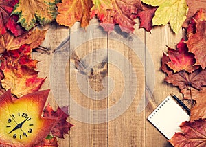 Still life of maple leaves, clock, notepad and pen.