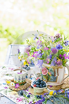 Still life with meadow flowers bouquet, berries and cup of tea in natural light outdoors, vivid wild flowers, berries on table