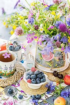 Still life with meadow flowers bouquet, berries and cup of tea in natural light, vivid wild flowers, berries on table