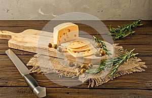 Still life on the morning table. Sliced cheese, olives and rosemary on a wooden kitchen board. Rustic style