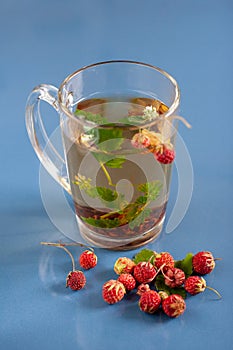 Still life of a mug of herbal tea on blue ceramic tiles with dust texture and reflection. Near scattered strawberries. Focus on th