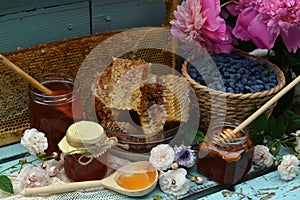 Still life with natural honey, honeycomb cut in pieces and honeysuckle berry with flowers on wooden background outside.