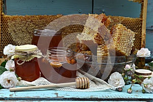 Still life with natural honey in jar, dipper, flowers and stick on wooden background outside. Countryside summer rural background