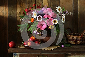 still life with nectarines and garden flowers in a clay jug on a dark background.