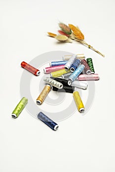 A still life with a number of spools of colored thread on a white surface and a bouquet of dried plants