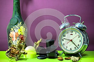Still life with old broken alarm clock, old glass vase, dead rose, negative film, green golf, colorful background