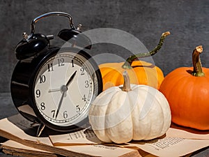 Still life with old fashion alarm clock, pumpkins and old book on dark background